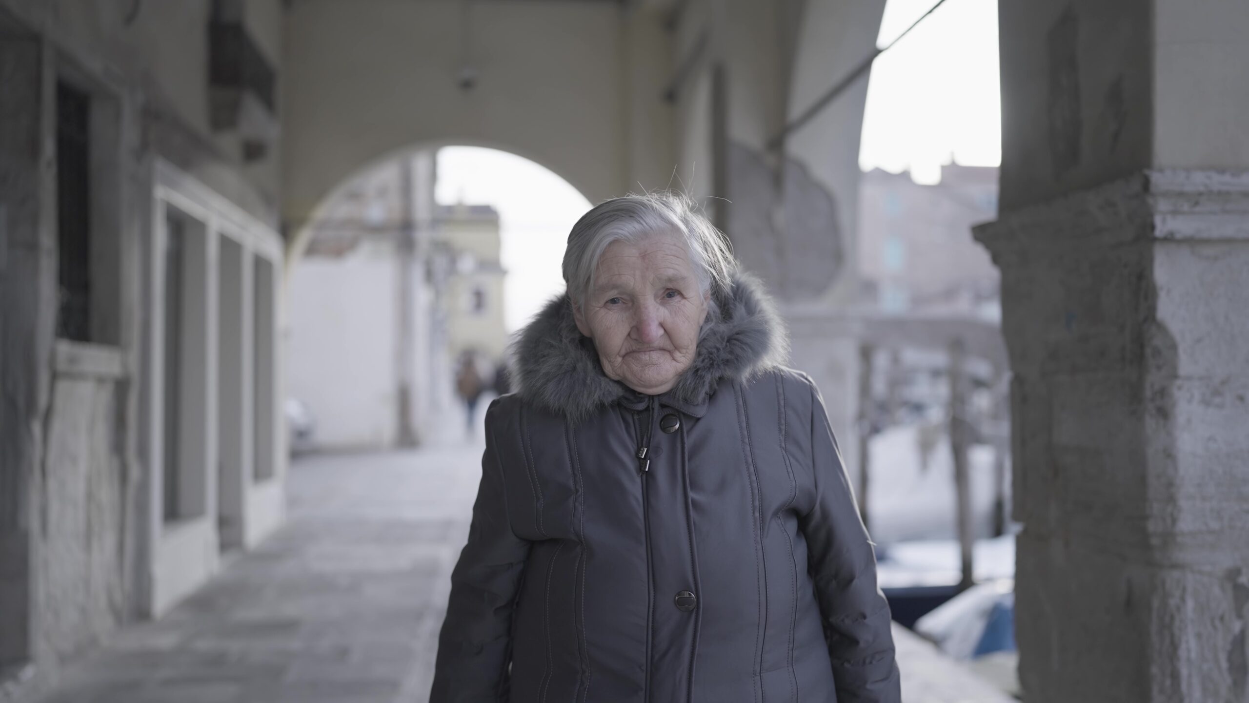 Donna anziana in cappotto sotto un antico edificio