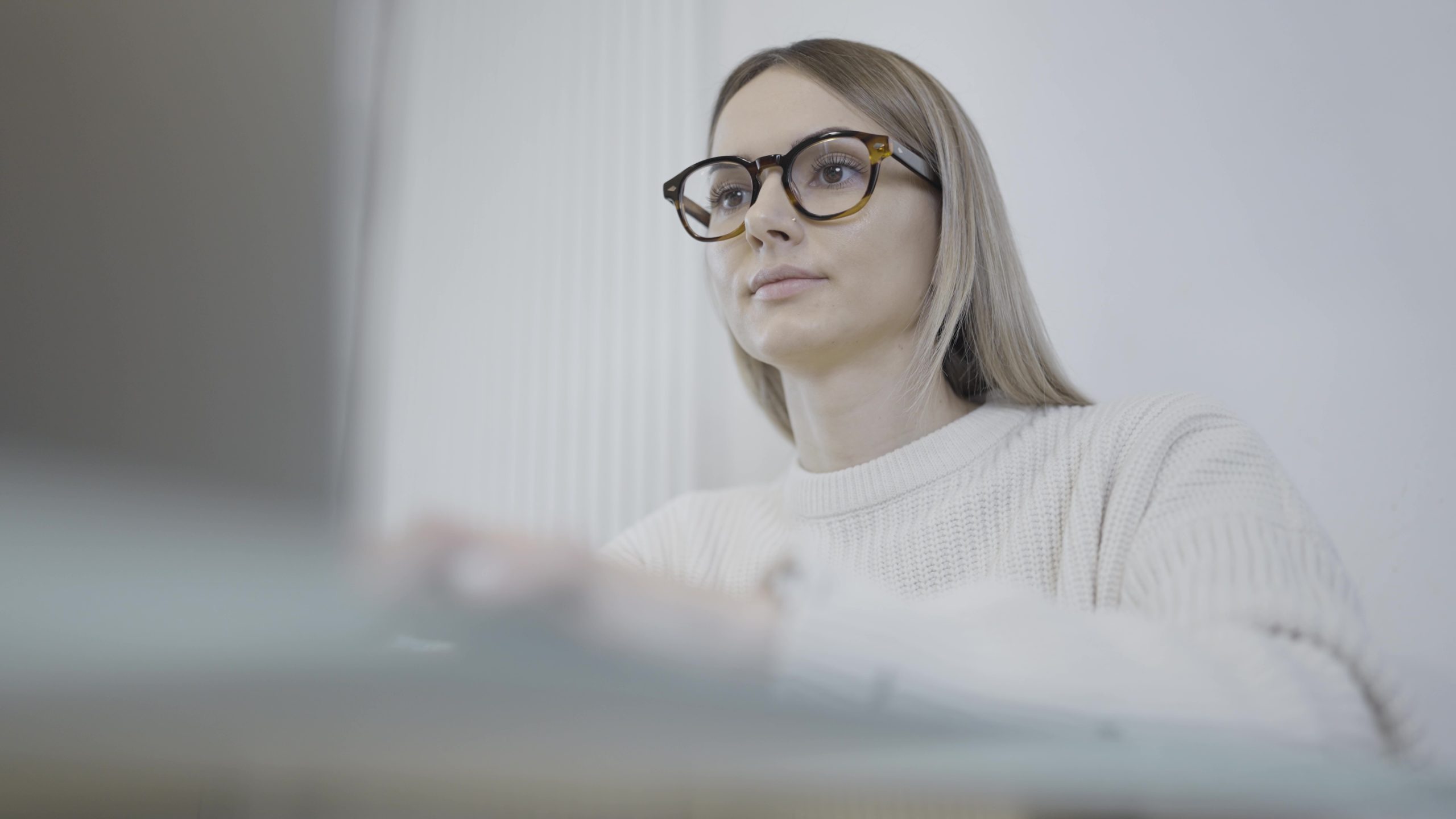 Una donna felice con gli occhiali siede alla scrivania e sorride mentre lavora su un laptop