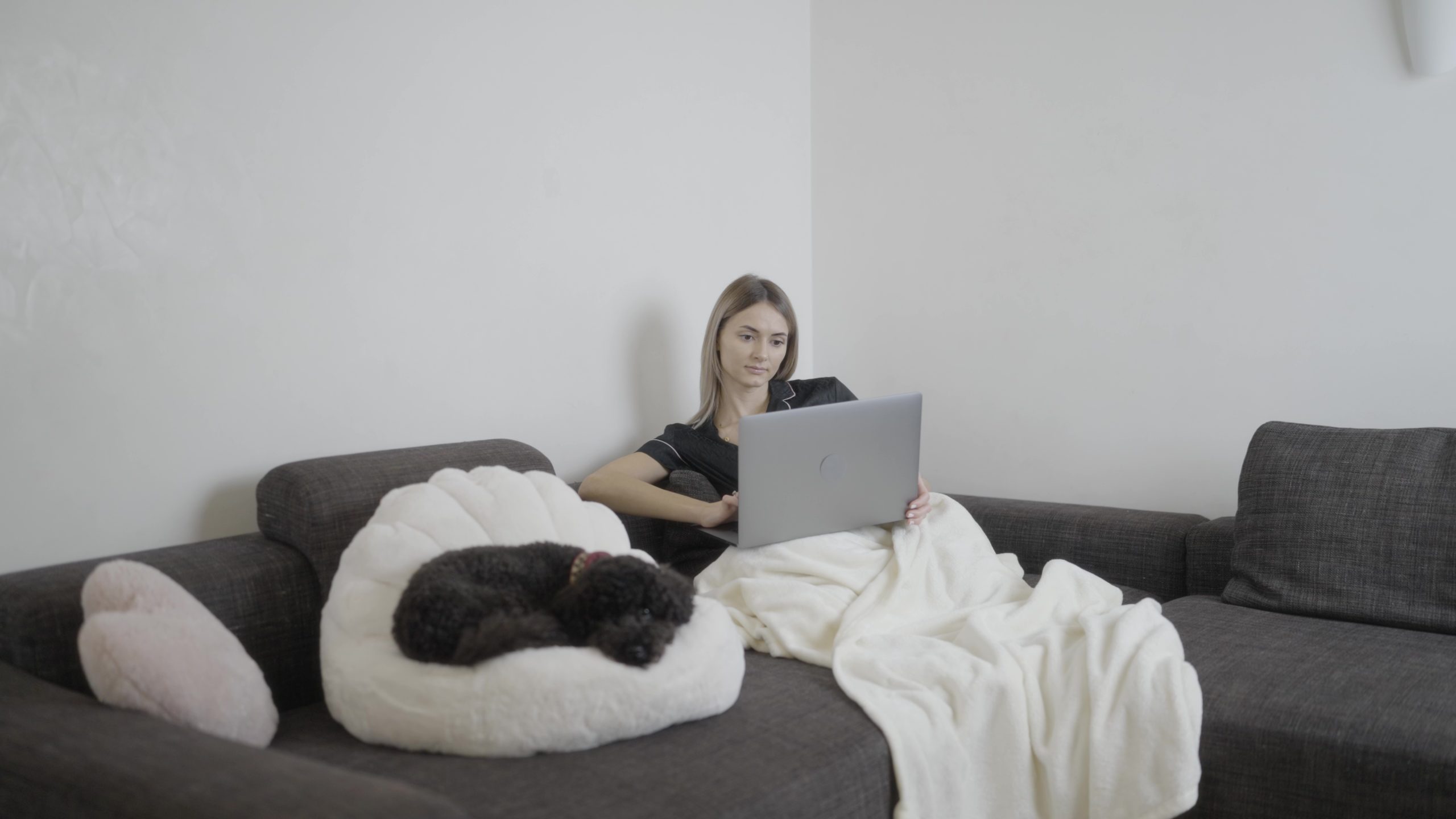 A woman is comfortably sitting on a couch with a laptop in a house