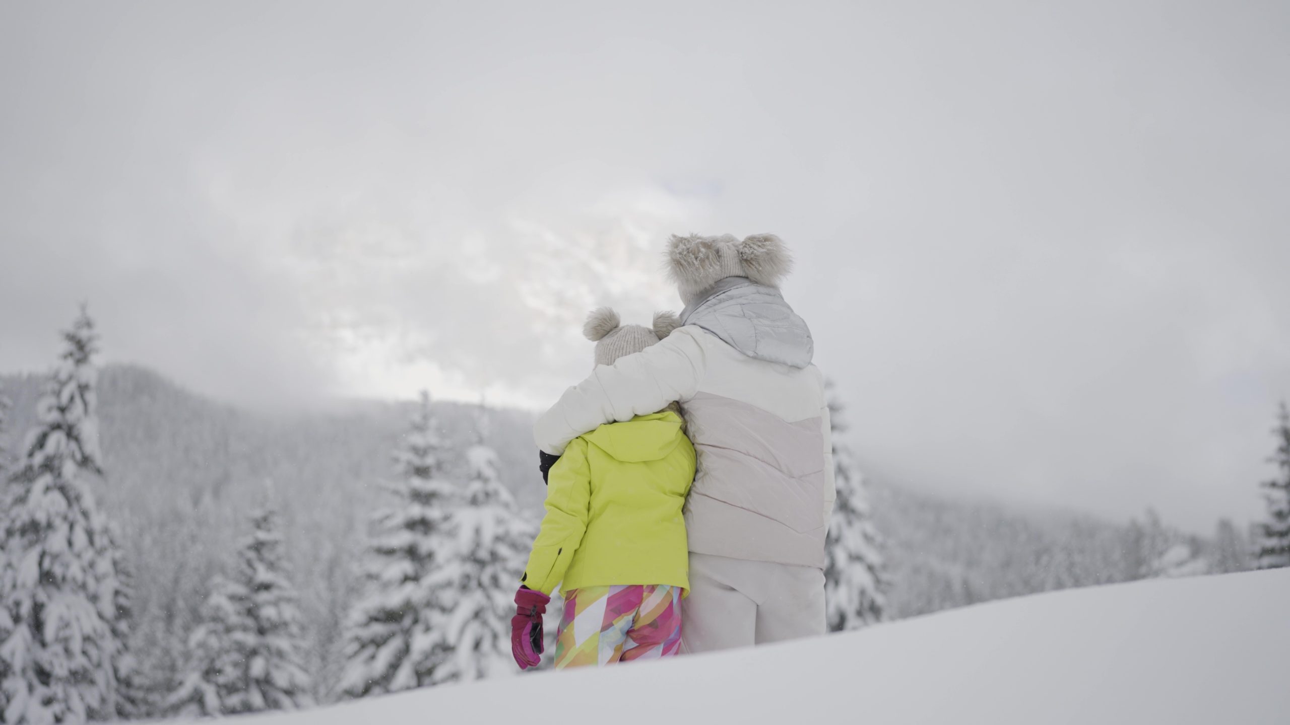 Mamma e figlia guardano bosco tra la neve sotto montagne alte