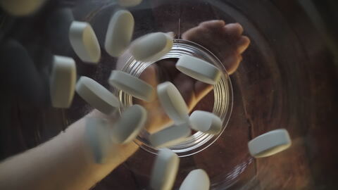 Pills Falling into a Jar with Hand in Background