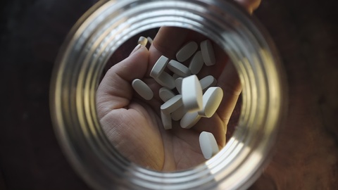 Hand Holding White Pills Through a Jar Opening